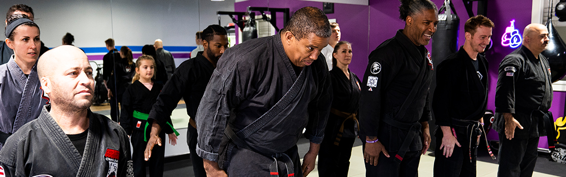 A group of people in black karate uniforms are standing in a gym.