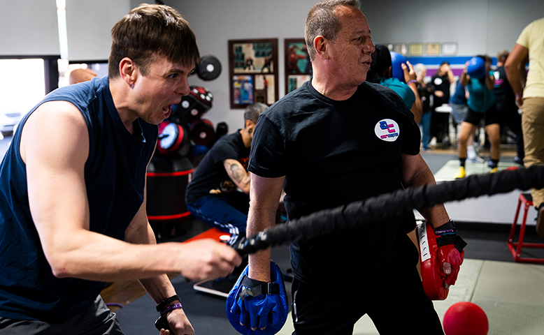 A man is teaching another man how to box in a gym.