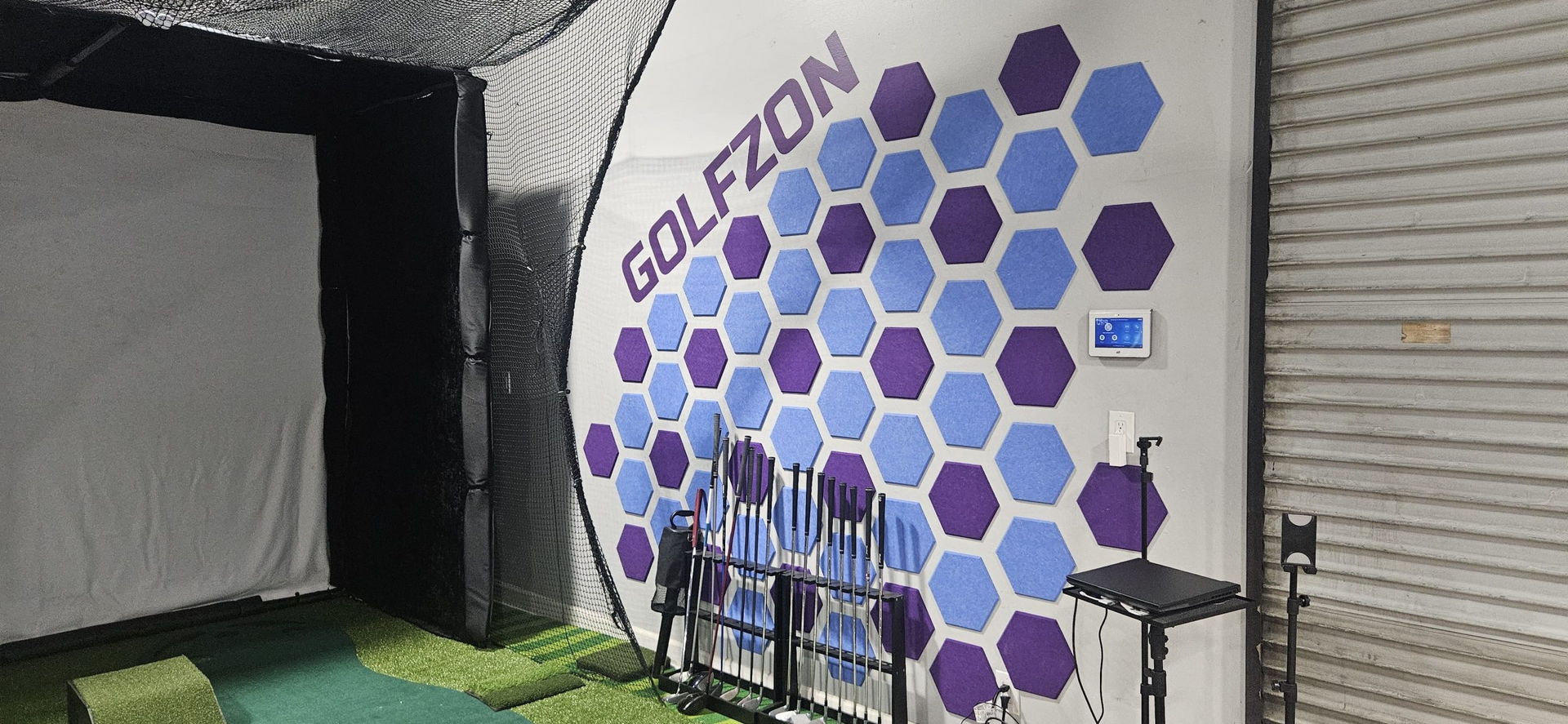 A golf simulator with a purple and blue mural on the wall.