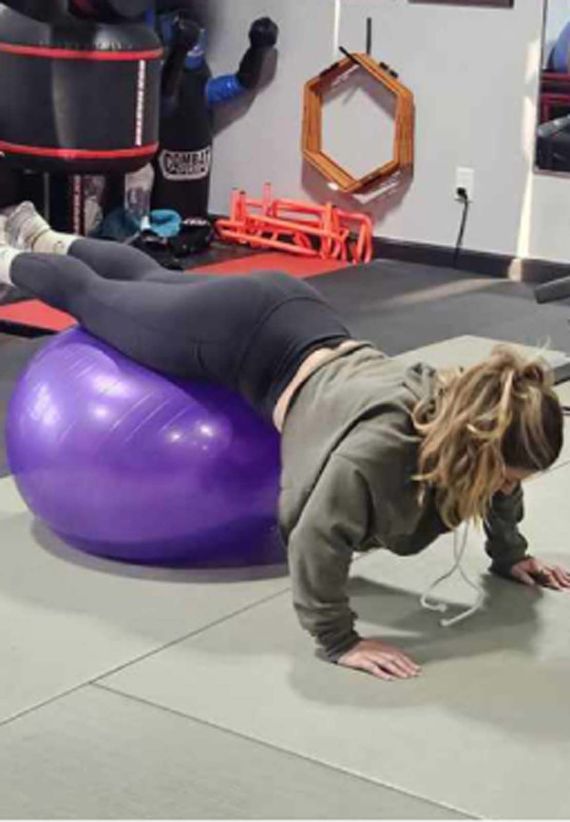 A woman is doing push ups on a purple exercise ball.