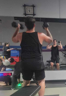 A man in a black tank top is lifting dumbbells in a gym