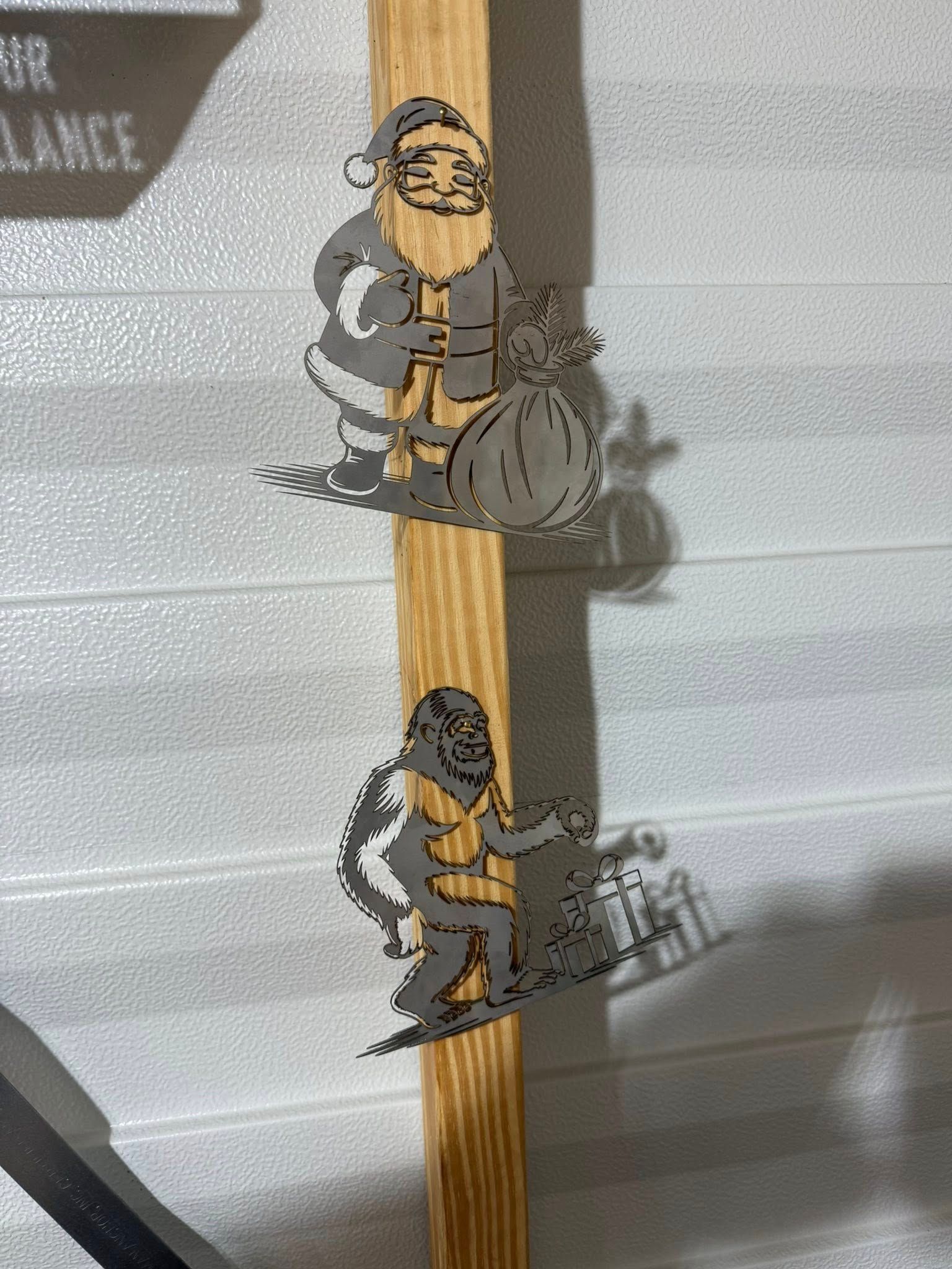 Santa and Bigfoot silhouettes on a wooden plank. Santa carries a bag, Bigfoot skis.