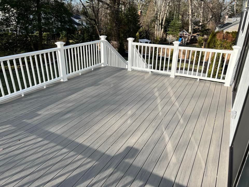 A large deck with a white railing and trees in the background.