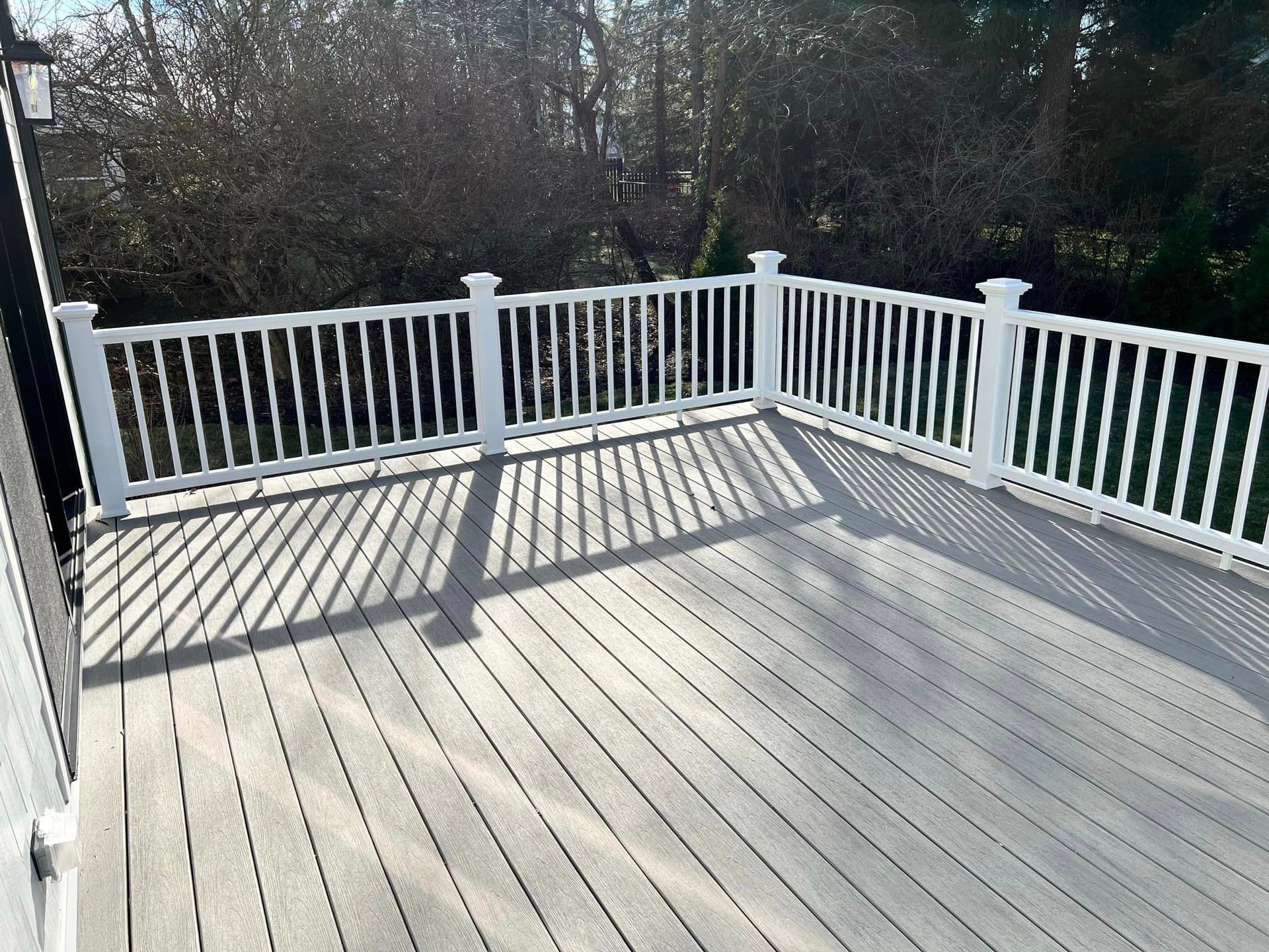 A large deck with a white railing and trees in the background.