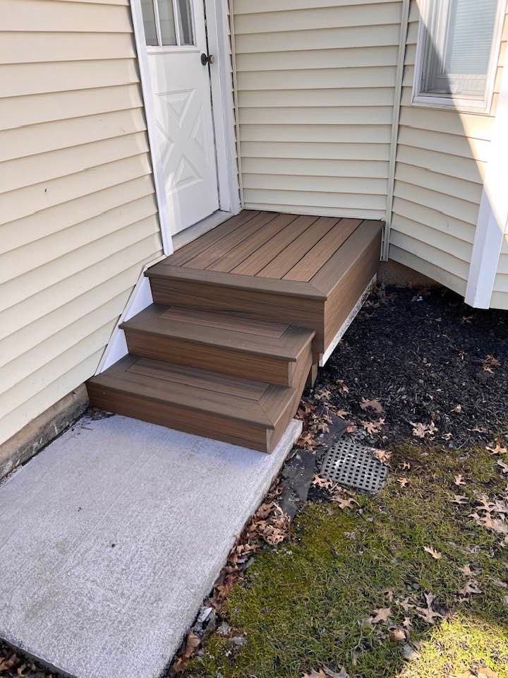 A wooden deck with stairs leading up to the front door of a house.