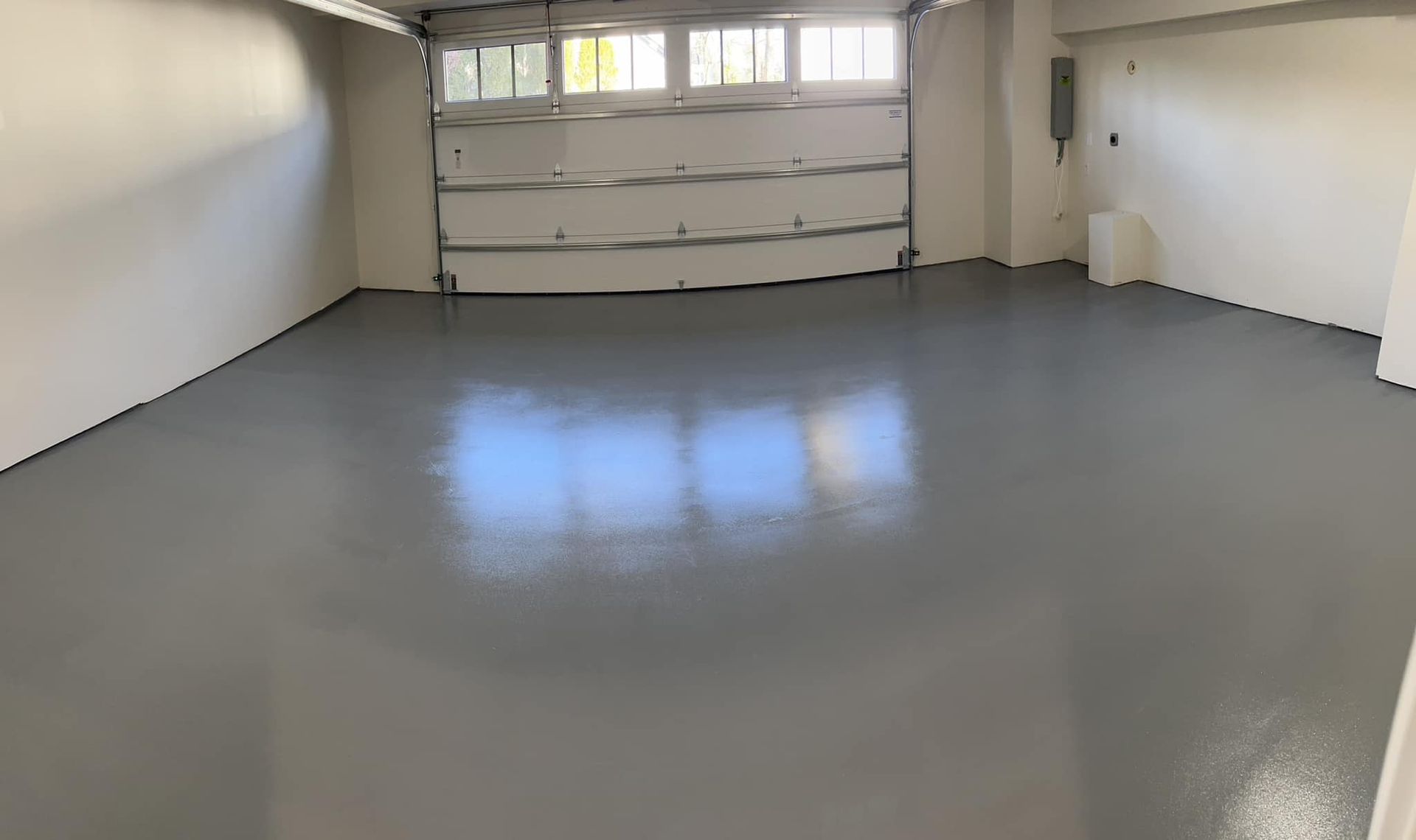 An empty garage with a garage door open and a gray floor.