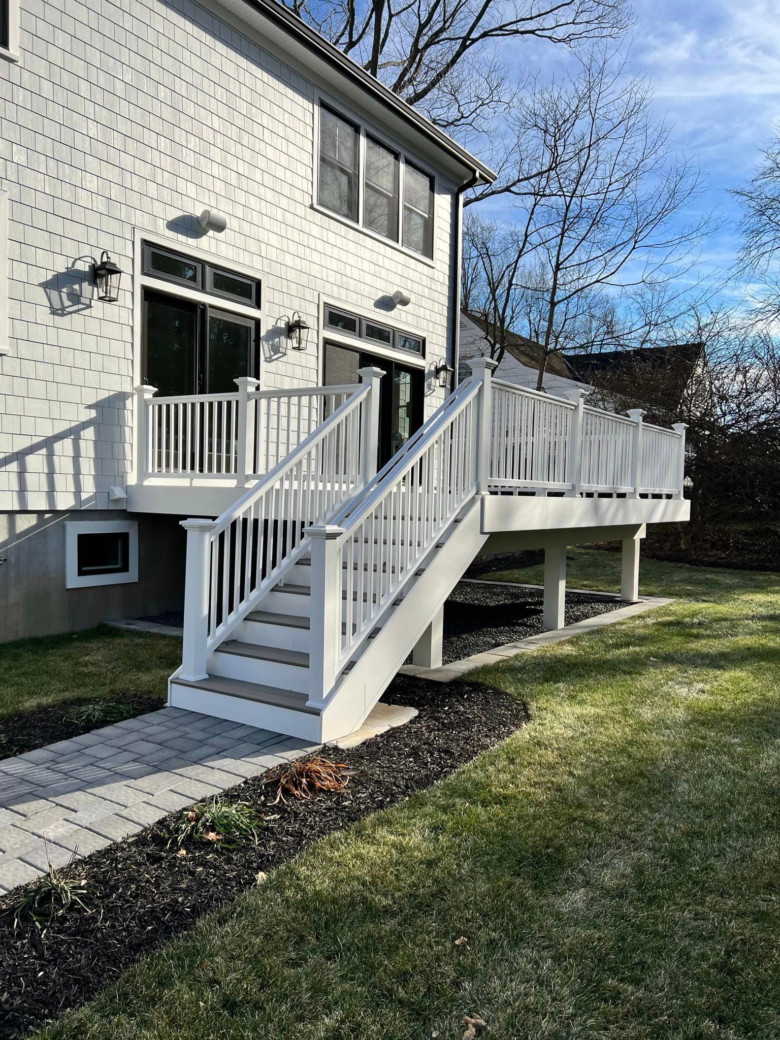 A white deck with stairs leading up to it is in the backyard of a house.