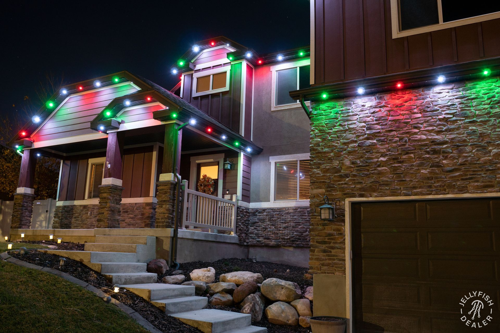 Permanent LED holiday lighting installed on a craftsman-style home in red, green, and white.