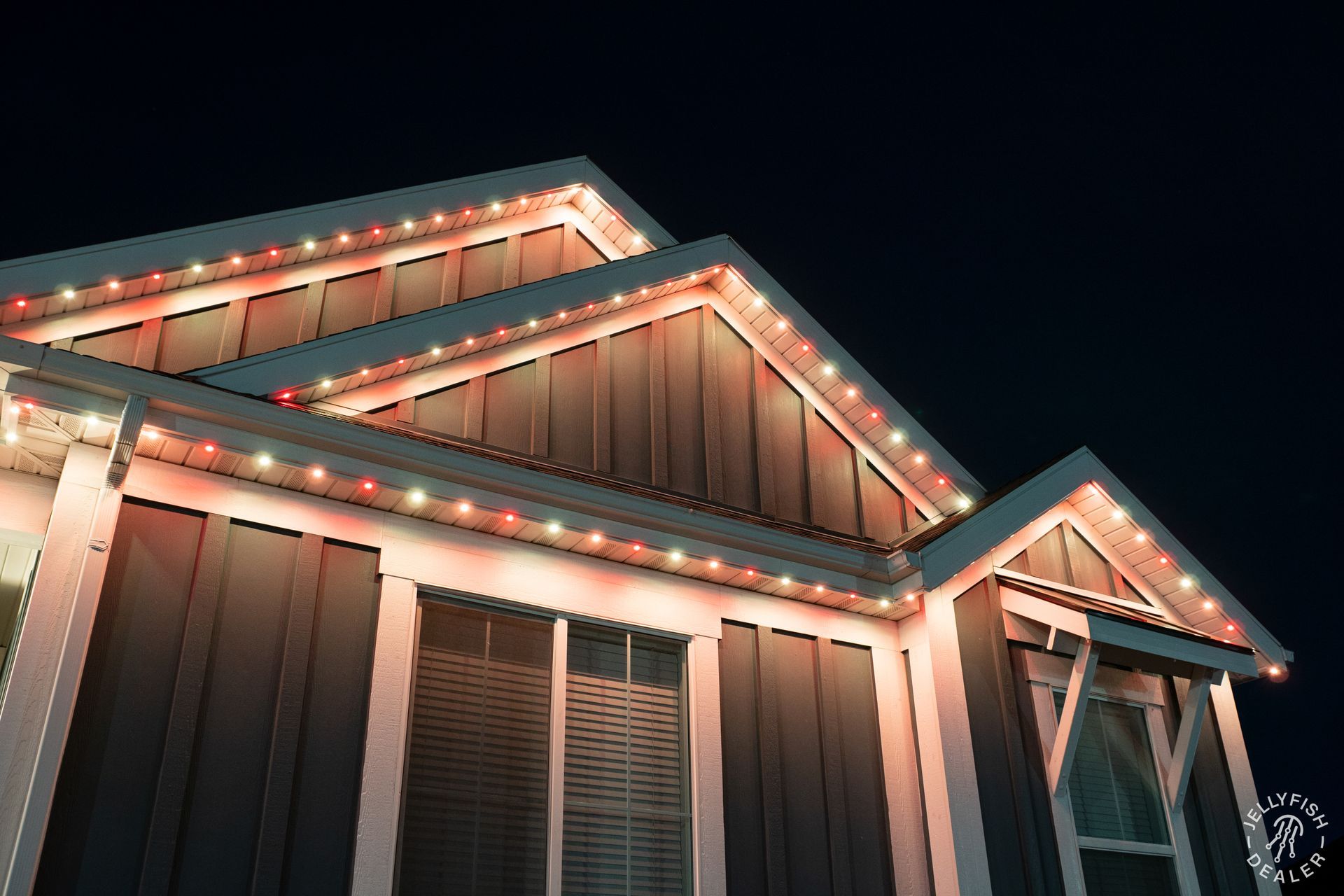 Close-up of JellyFish Lighting installed along roof peaks of a modern farmhouse, glowing in warm red