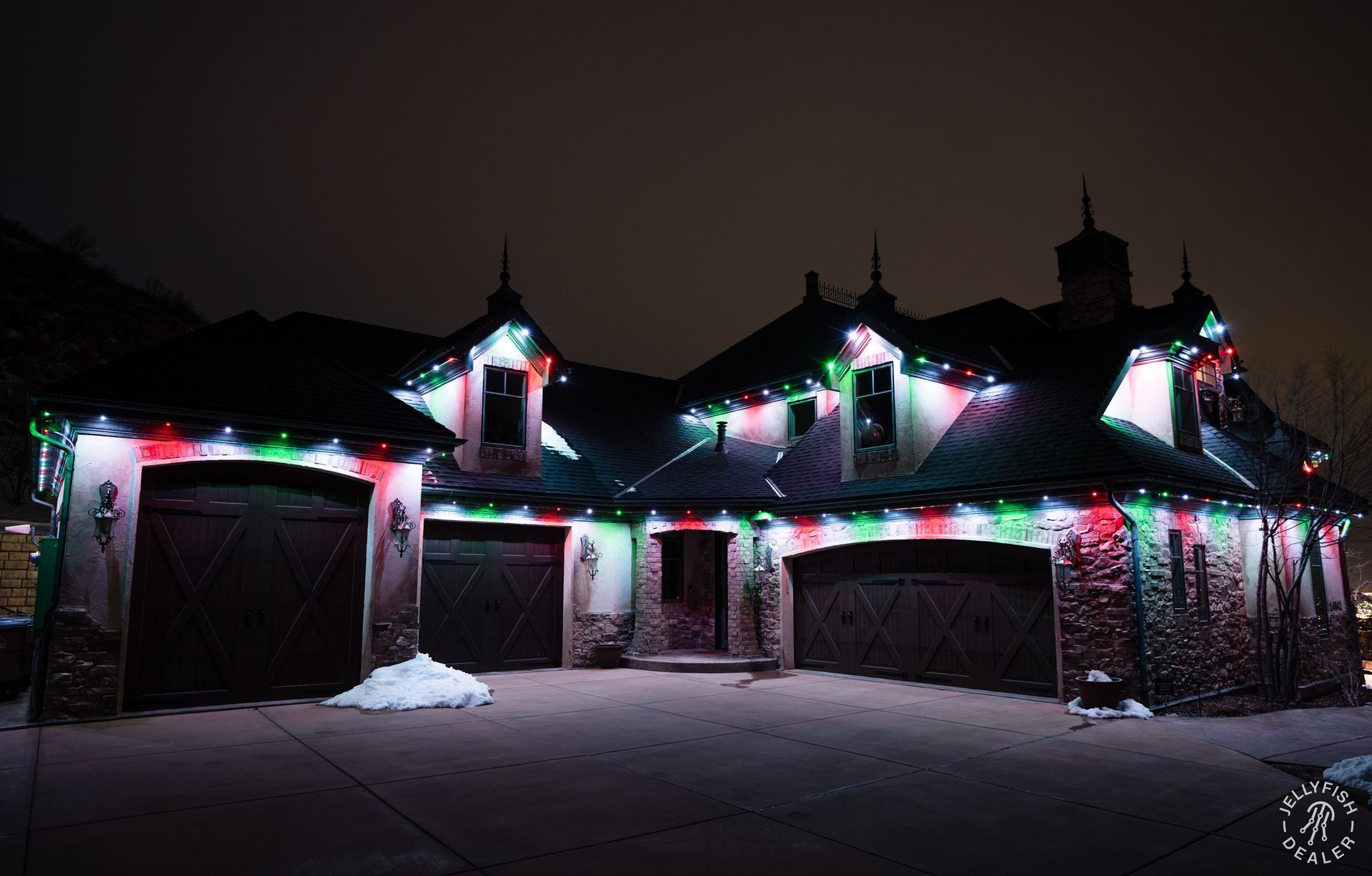 Luxury home illuminated with JellyFish permanent Christmas lights in red, green, and white.