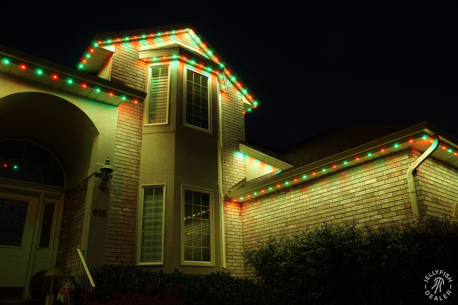 Permanent holiday LED lights glowing in warm red and green tones along a home’s roofline.
