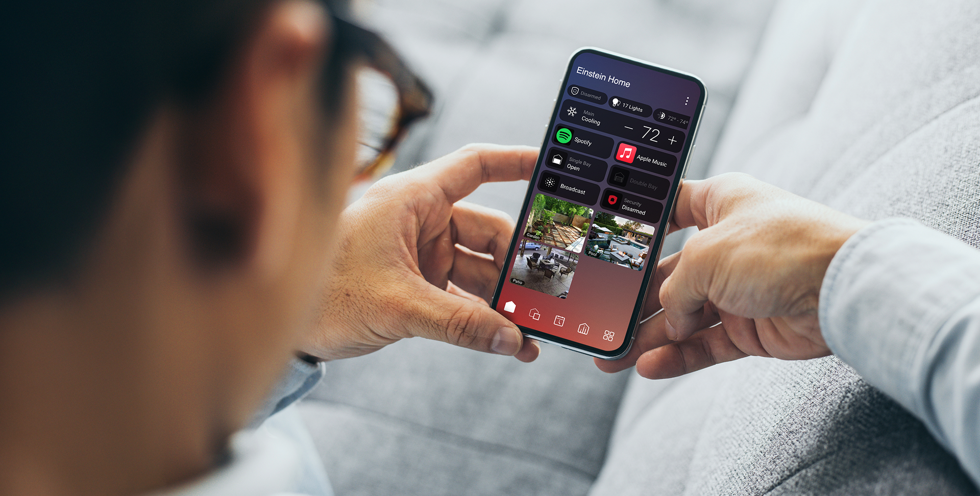 Person holding a smartphone showing a smart home interface with climate, lighting, and camera controls.