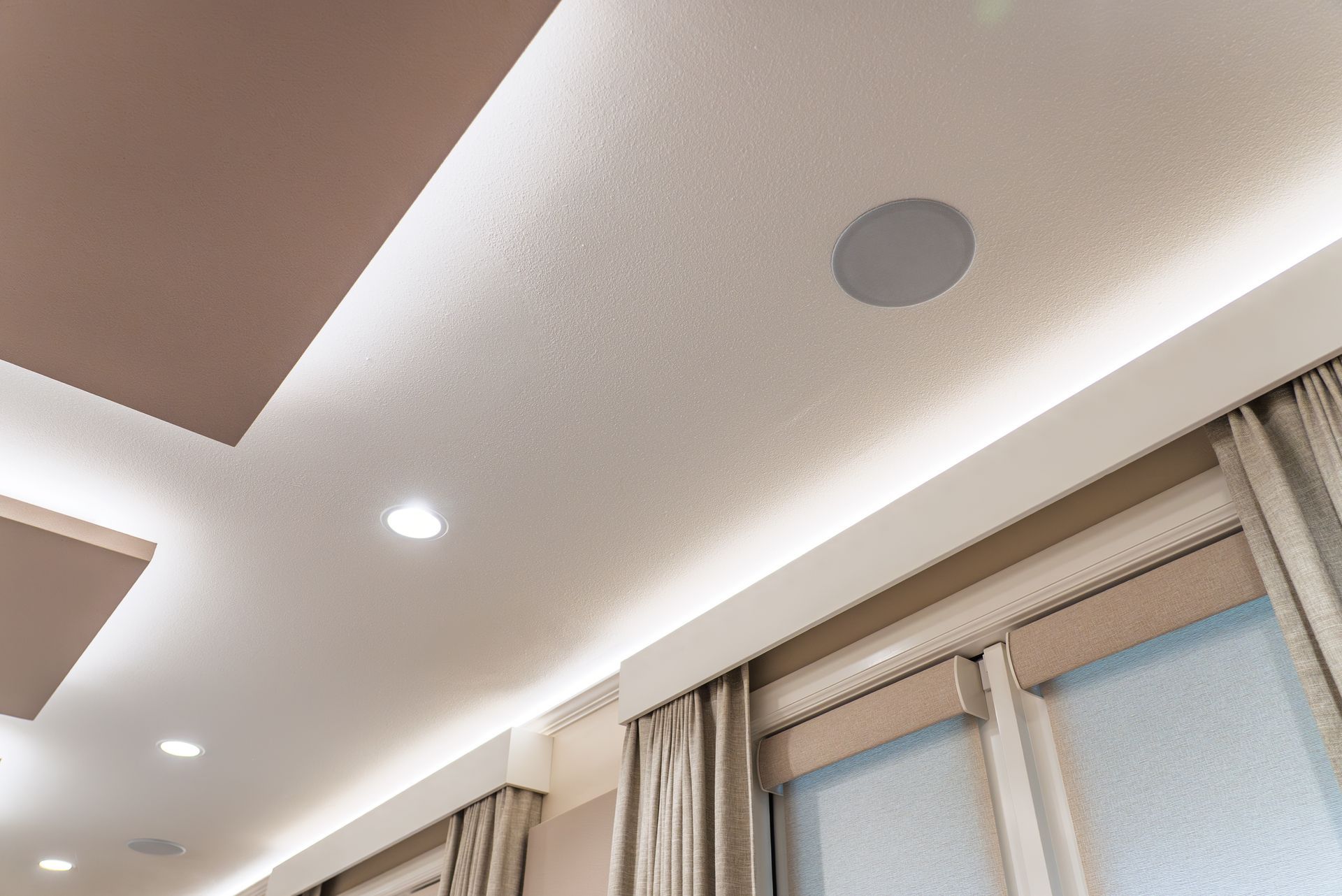 Recessed ceiling lights and soft cove lighting in a modern room with curtains.