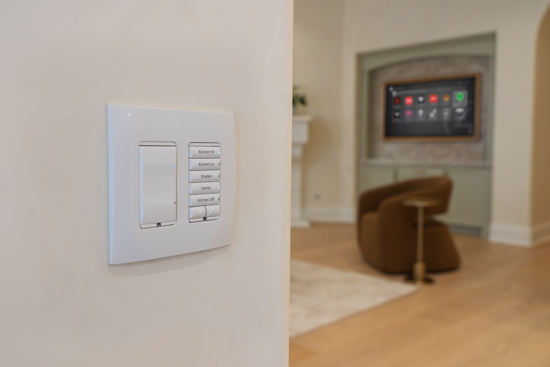 Smart home keypad and light switch on a wall with a home theater in the background.