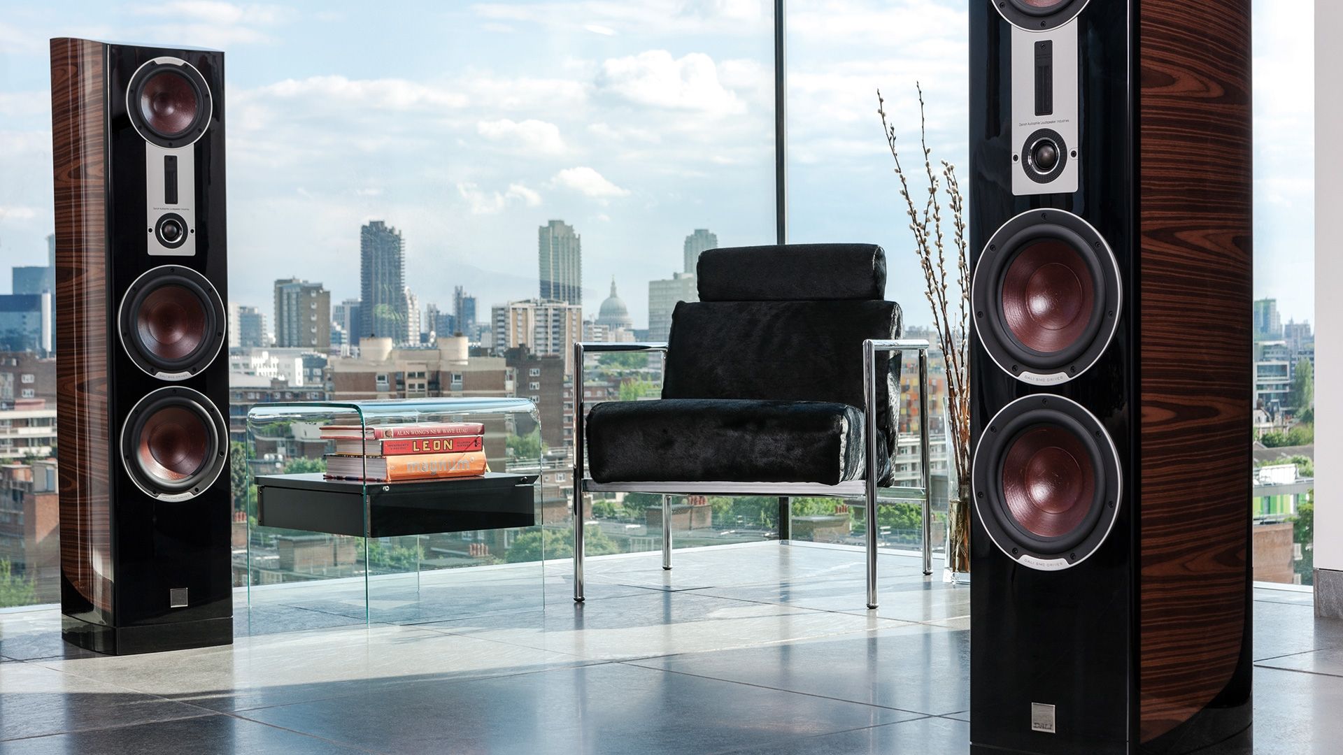 High-end DALI floor-standing speakers positioned in front of large windows overlooking a city skyline.