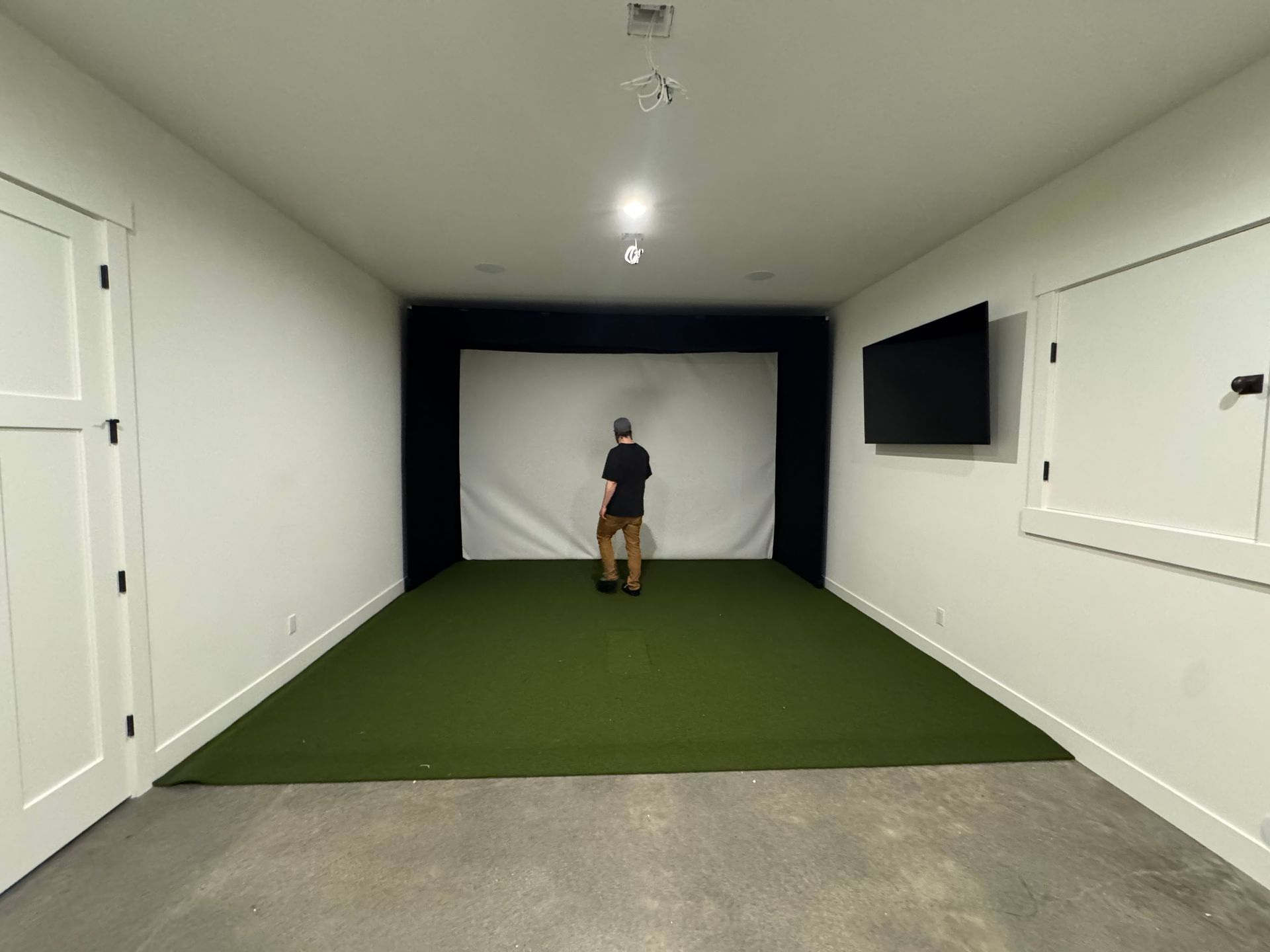Indoor golf simulator room with impact screen side display and turf near completion