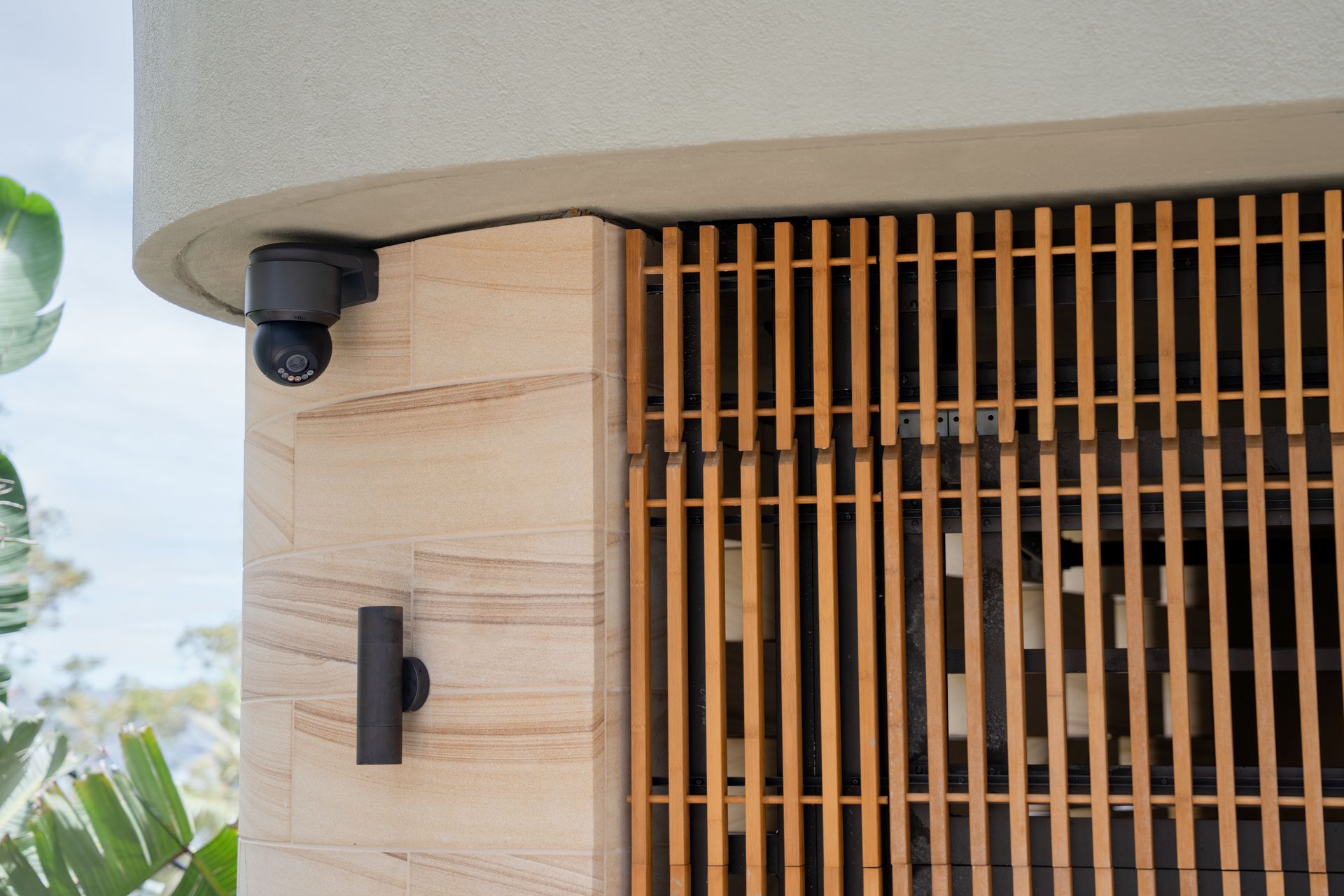 Exterior security camera mounted on the corner of a modern home overlooking an entry area.