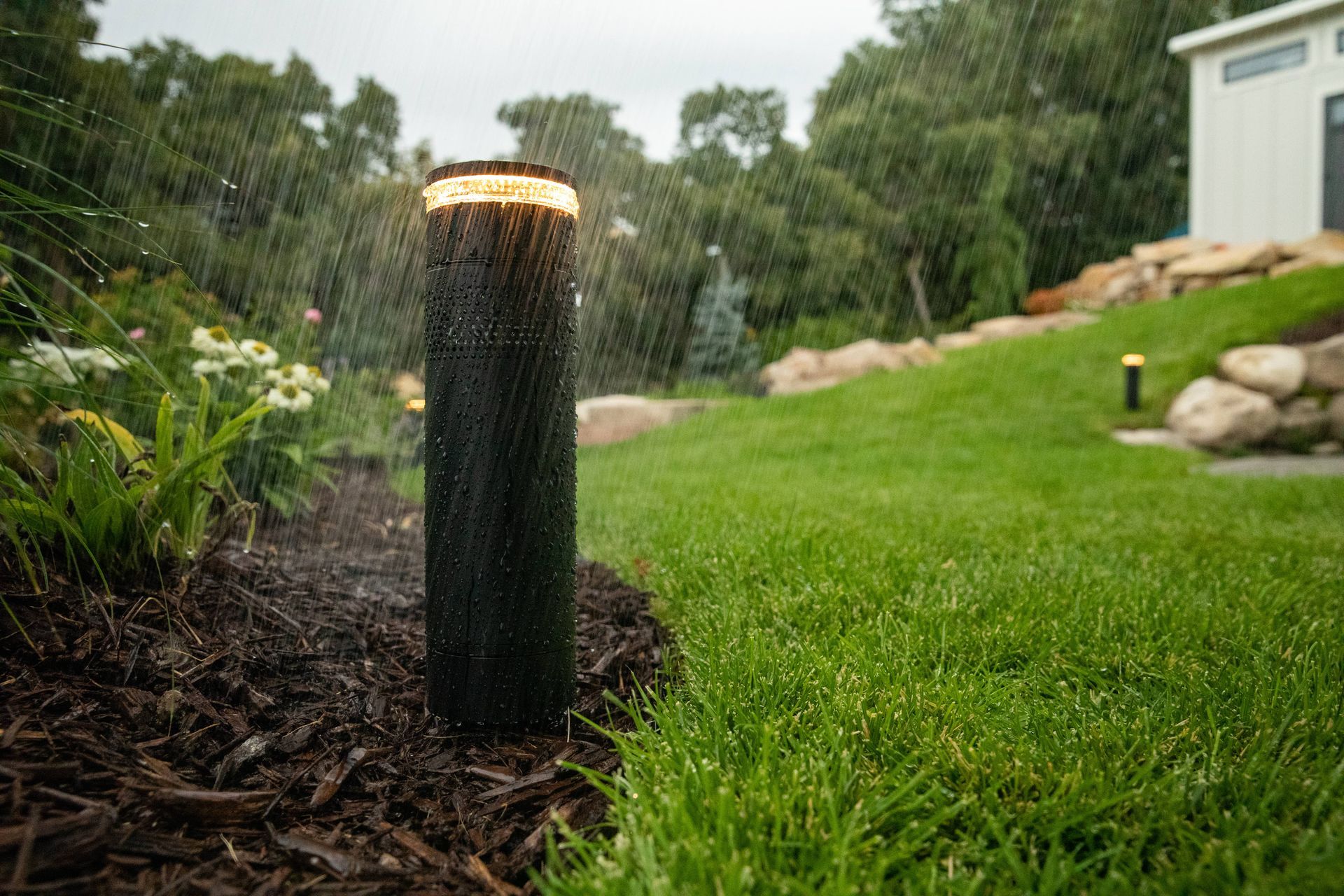 Outdoor lighting bollard in rain illuminating landscape path