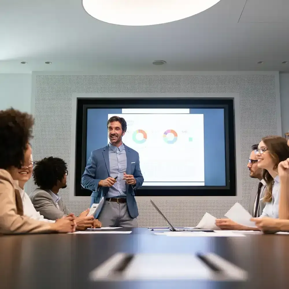 Man presenting financial data on a screen to a group in a conference room.