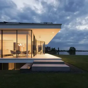 A modern house with a lot of windows overlooking a lake