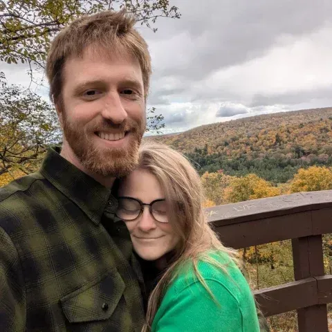 A man in a plaid shirt is hugging a woman in a green shirt.