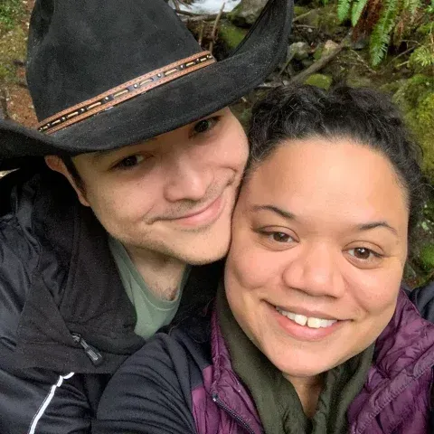 A man and a woman are posing for a picture together . the man is wearing a cowboy hat.