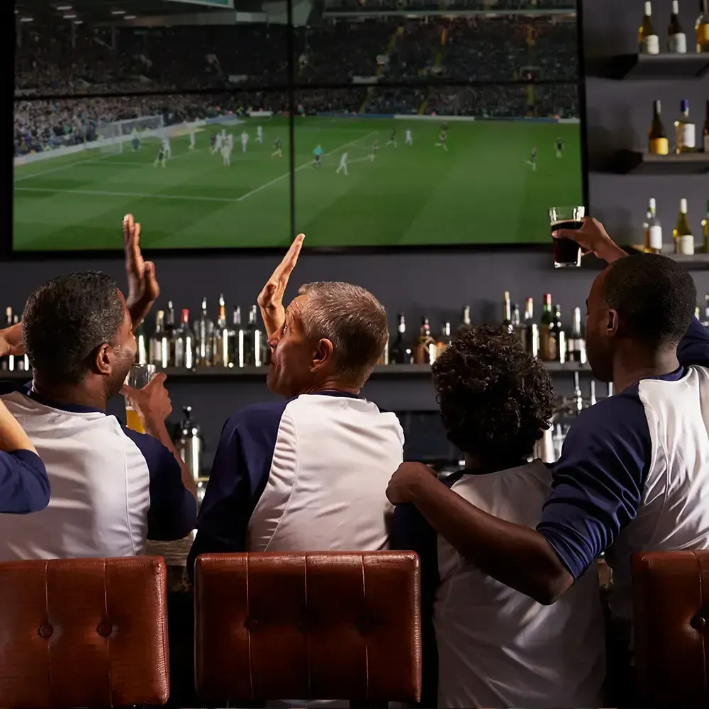 People cheering at a bar watching a soccer game on multiple screens.