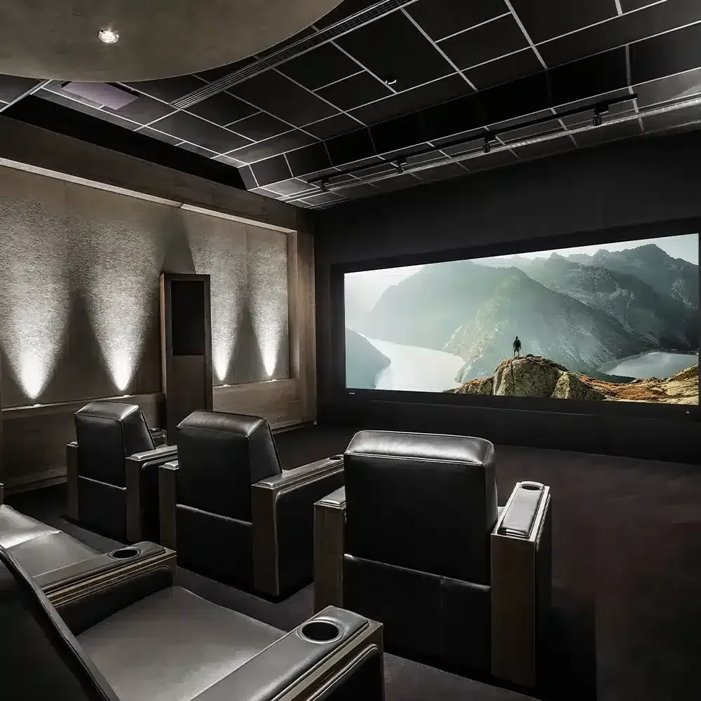 A luxury home theater with black leather recliners, large screen displaying a mountain scene, and dim lighting.
