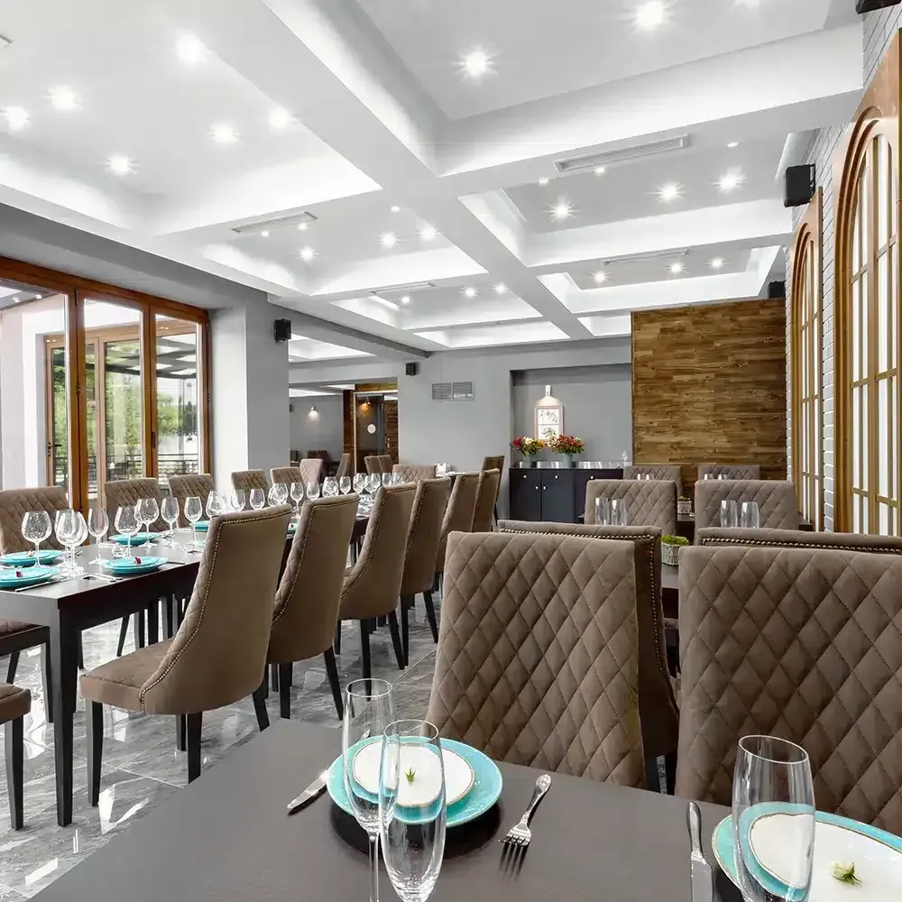 Restaurant interior with tables set for dining; brown chairs, blue plates, and large windows.