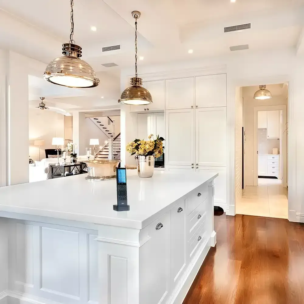 Kitchen with white island and cabinets, two pendant lights, and a remote control on the island.