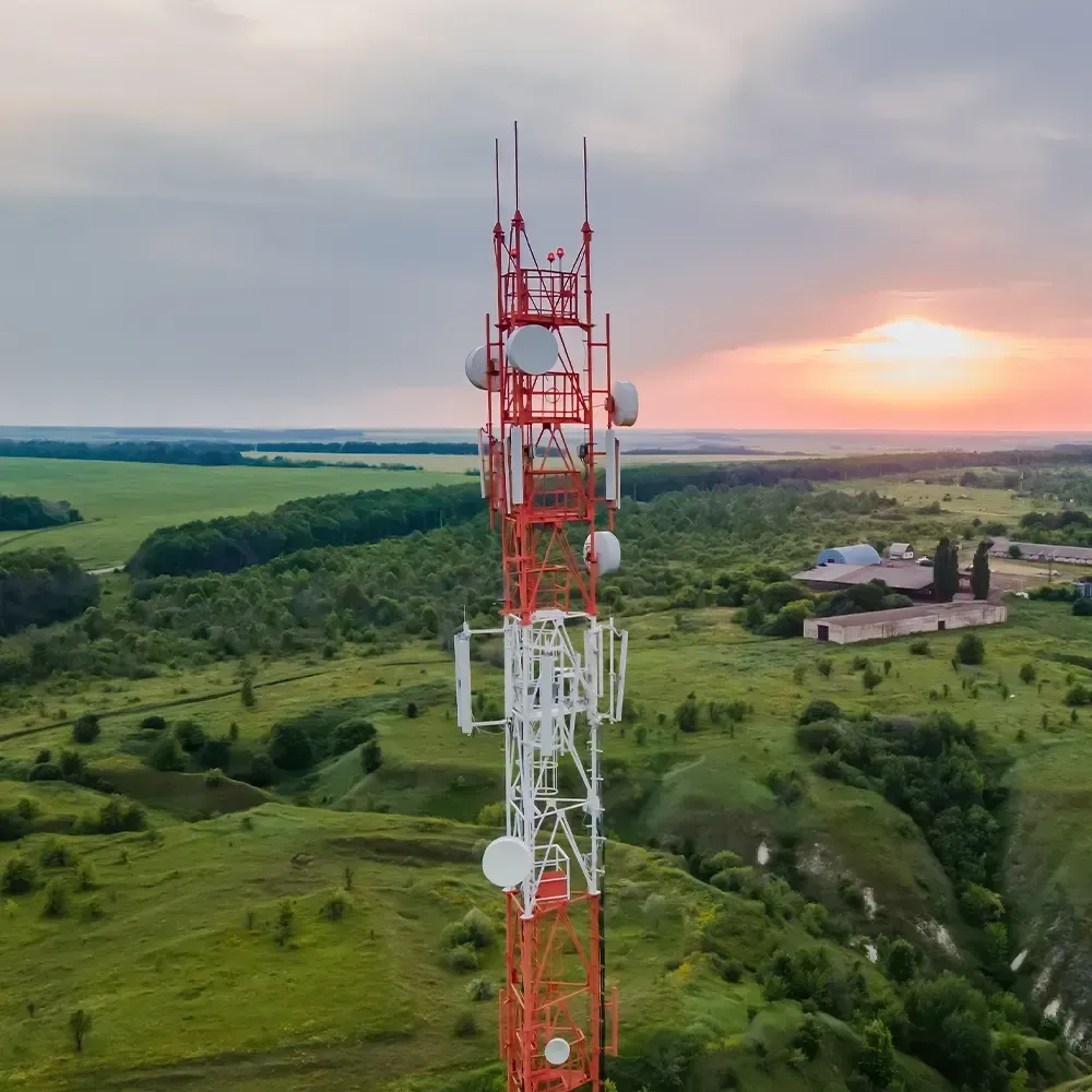 Cell tower against a sunset backdrop, in a green field. The tower is red and white.