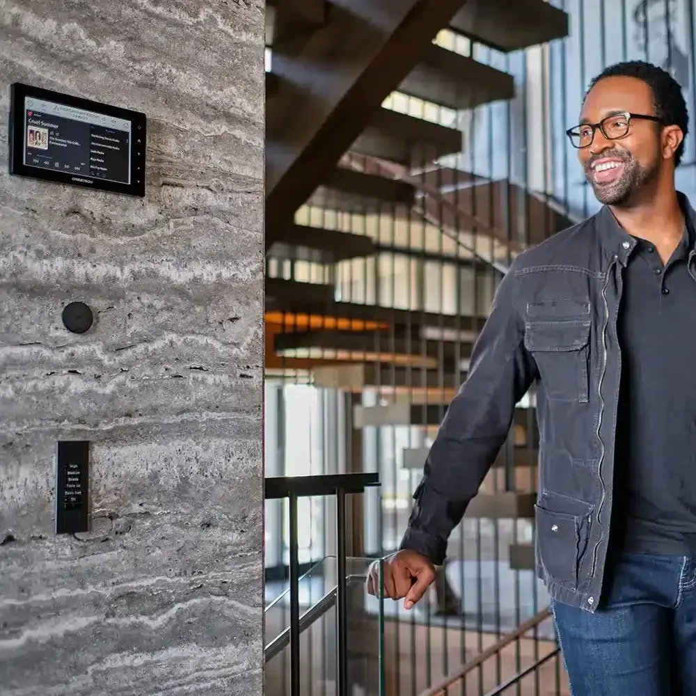 Man by a staircase, looking toward a control panel on a textured wall.