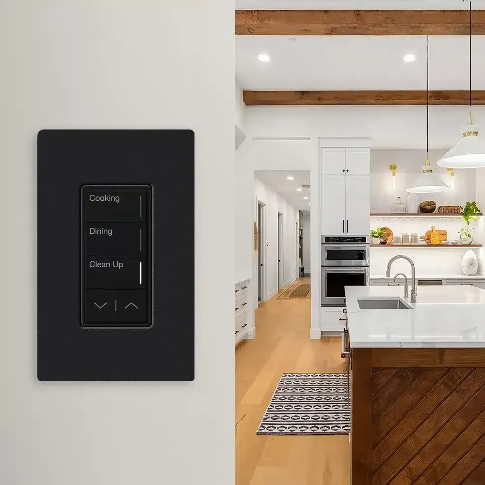 Black smart light switch on white wall with kitchen in background.