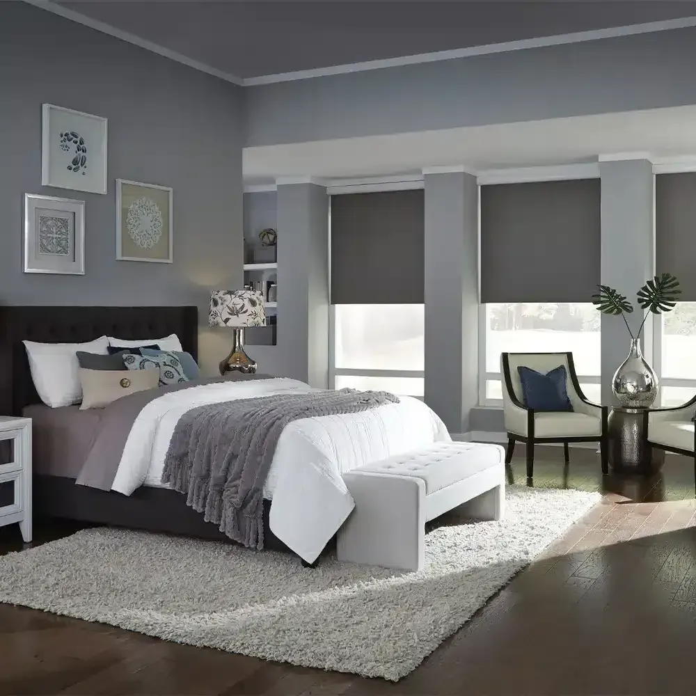 Bedroom with gray walls, bed, windows with blinds, bench, chair, and rug.