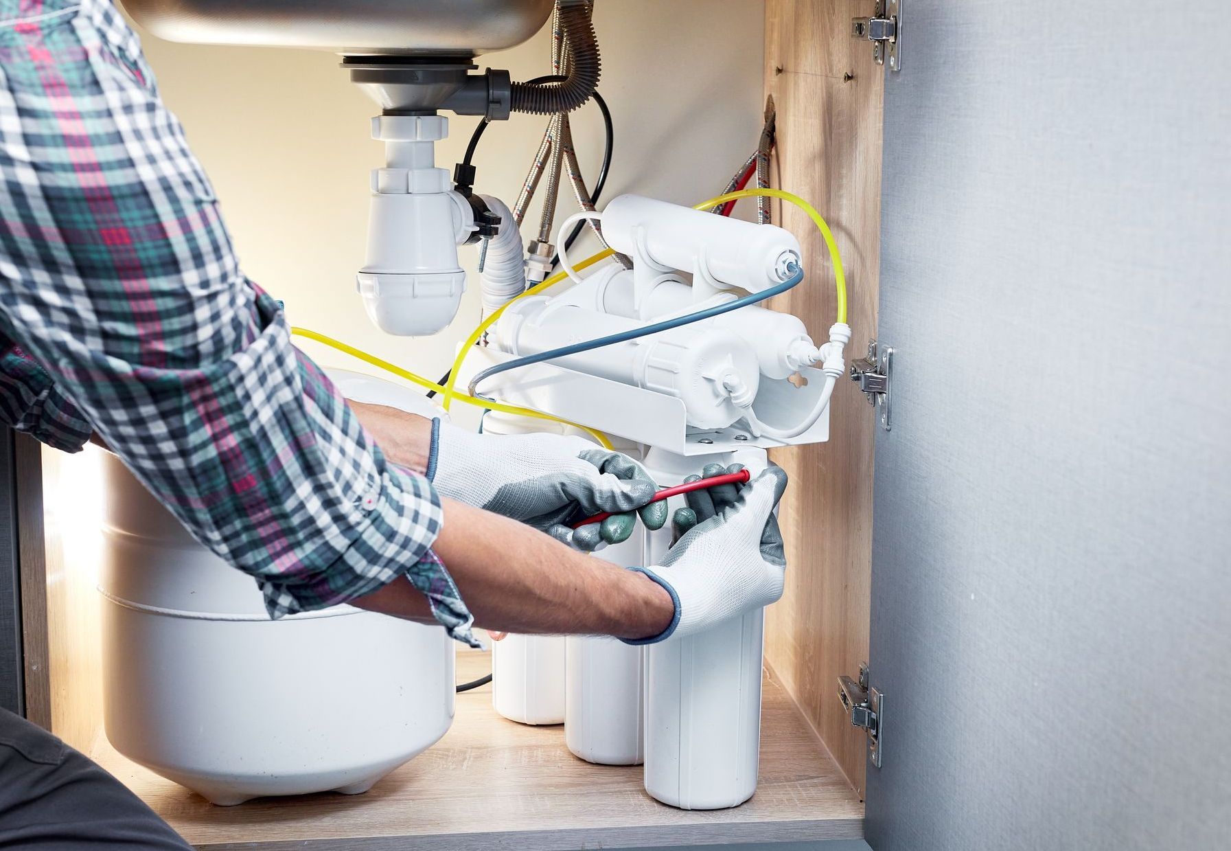 A man is fixing a water filter under a sink.
