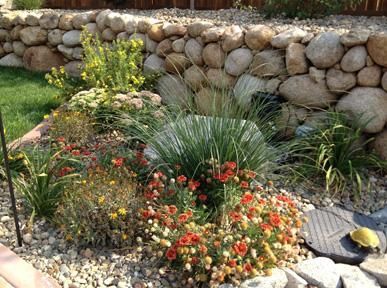 A garden with flowers and rocks in front of a stone wall.