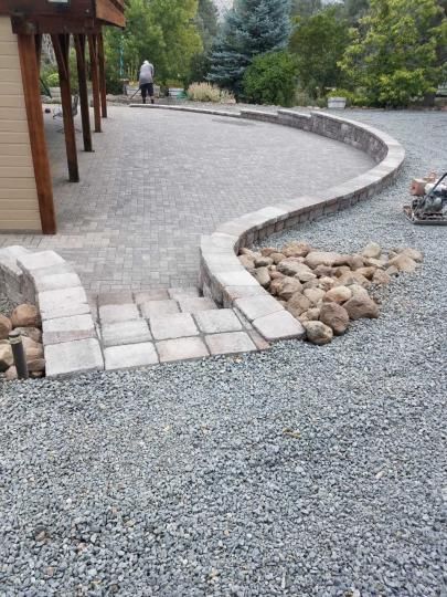 A gravel driveway with a stone wall and steps leading to a house.