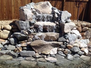 A waterfall is surrounded by rocks and a wooden fence.