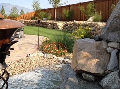 A waterfall in a backyard with a fence in the background