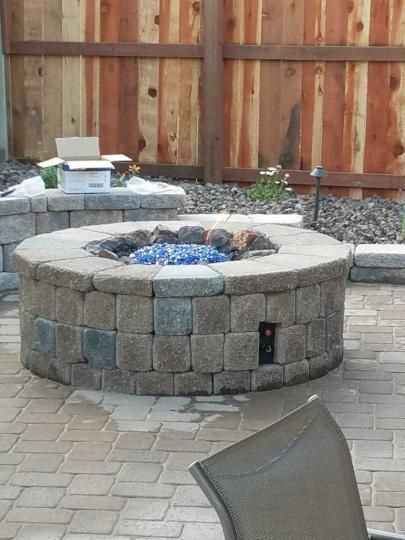 A fire pit is sitting on a brick patio next to a wooden fence.