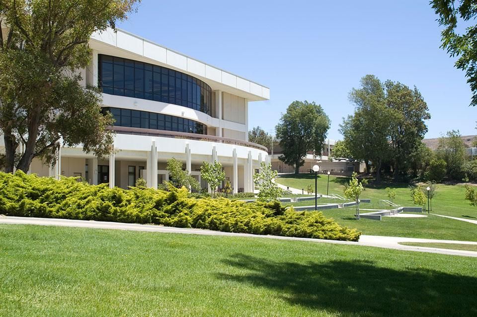 A large building with a lot of windows is surrounded by grass and trees