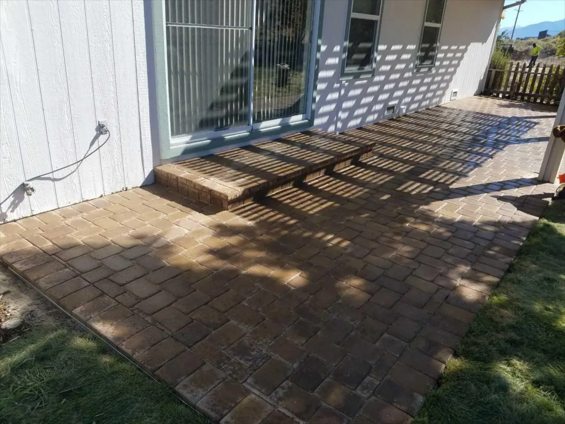 A brick patio in front of a house with a sliding glass door.