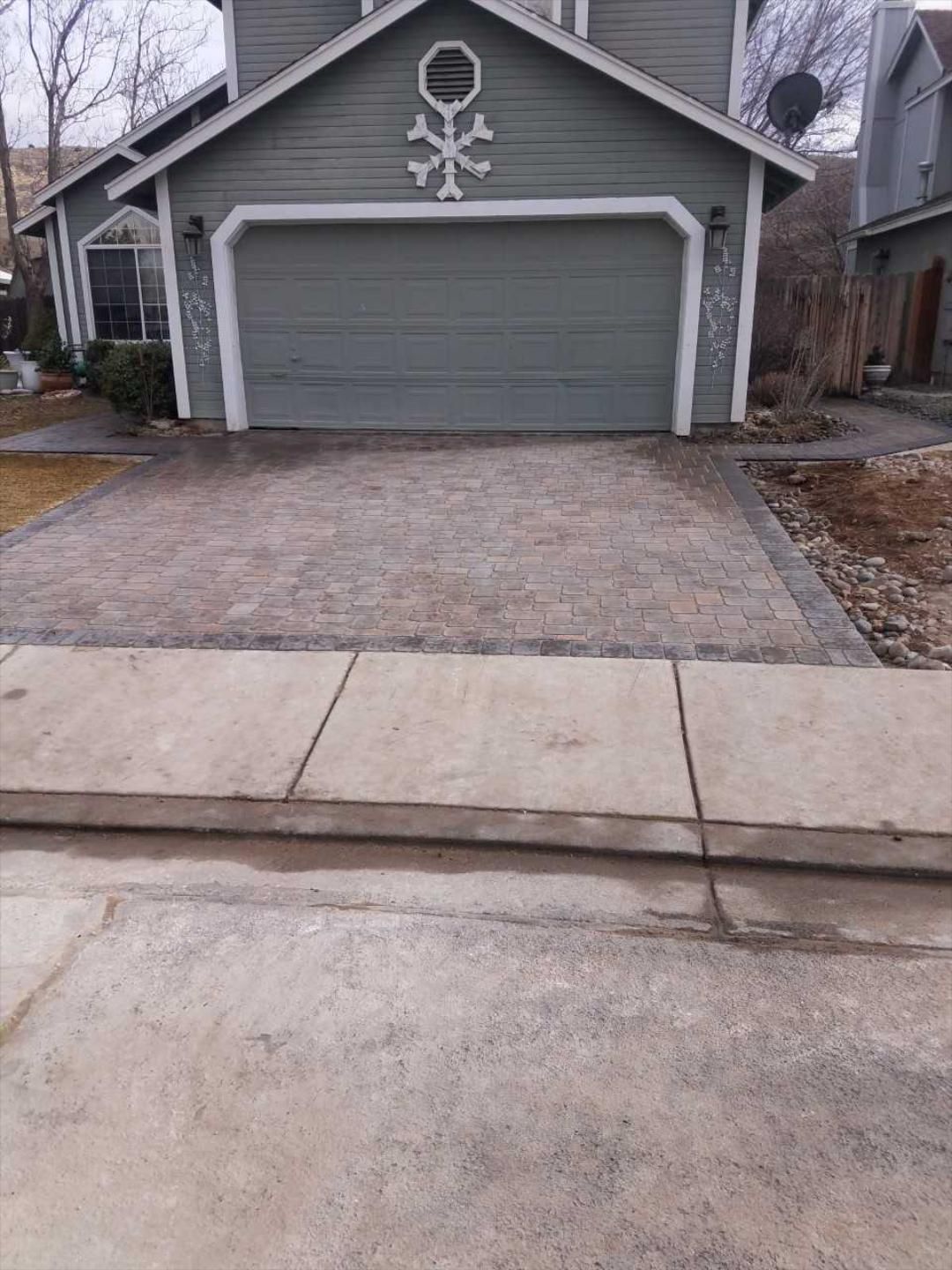 A house with a gray garage door and a brick driveway in front of it.