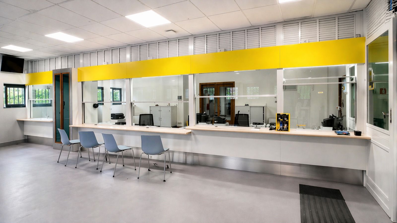 In un ambiente moderno e luminoso, un banco del servizio clienti con quattro sedie blu e uno striscione giallo sopra delle pareti divisorie in vetro.