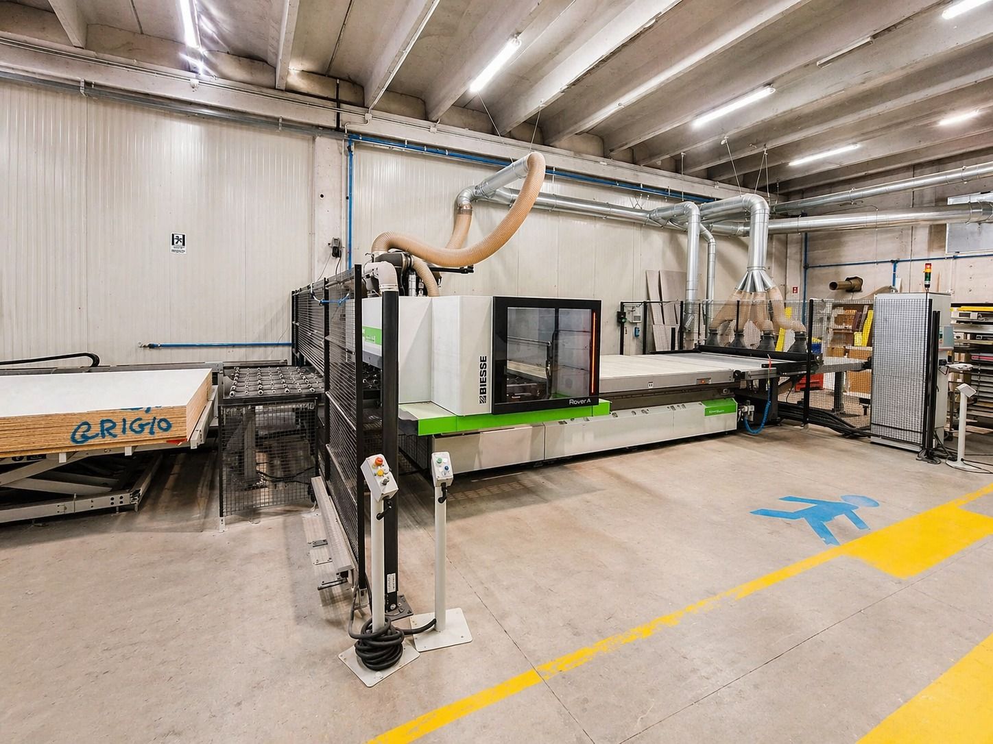 Una grande macchina a controllo numerico e i relativi materiali si trovano in un'officina industriale ben illuminata, con segnaletica di sicurezza dipinta sul pavimento.