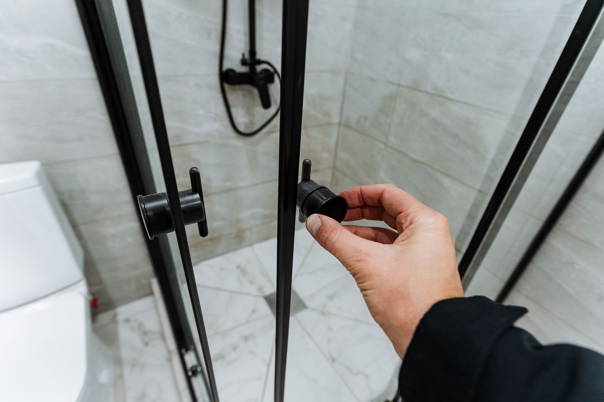 Hand removing hardware during shower door replacement on a modern framed glass shower.