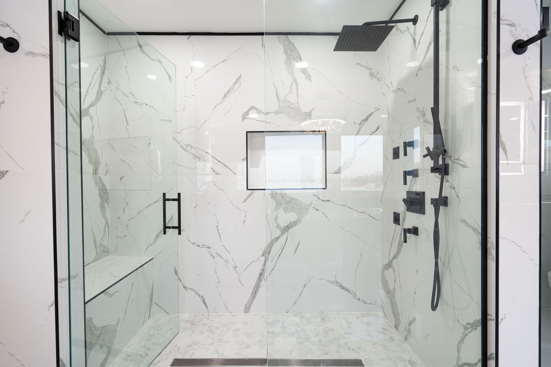 A marble-tiled shower with glass doors, a bench seat, a rainfall showerhead, and black fixtures A marble-tiled shower with glass doors, a bench seat, a rainfall showerhead, and black fixtures