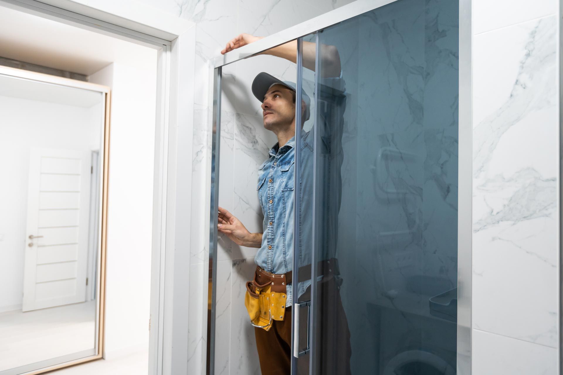 Workers are installing glass door of the shower enclosure.