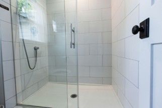 A tiled walk-in shower with a glass door, a handheld showerhead, and a white base A tiled walk-in shower with a glass door, a handheld showerhead, and a white base
