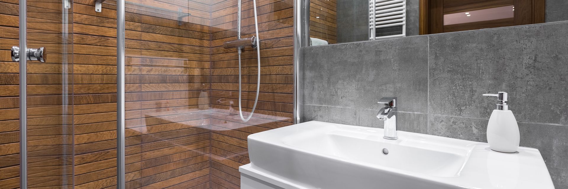 Modern bathroom with wood shower walls glass enclosure and sleek white sink for home renovation.